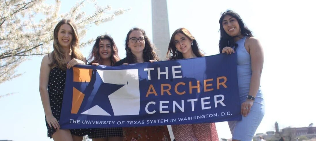 A group of young women hold the Archer Center banner with the Washington Monument in the background