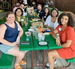 A group of alumni sit together at a picnic table at a gathering in Houston.