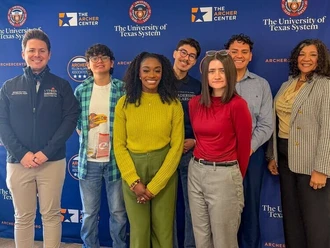 A group of Archer Fellows stand together in front of an Archer Center backdrop.